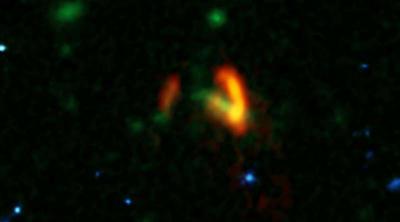 A composite image showing ALMA data (red) of the two galaxies of SPT0311-58. These galaxies are shown over a background from the Hubble Space Telescope (blue and green). The ALMA data show the two galaxies dusty glow. The image of the galaxy on the right is distorted by gravitational lensing. The nearer foreground lensing galaxy is the green object between the two galaxies imaged by ALMA.   <i>Credit: ALMA (ESO/NAOJ/NRAO), Marrone, et al.; B. Saxton (NRAO/AUI/NSF); NASA/ESA Hubble</i>